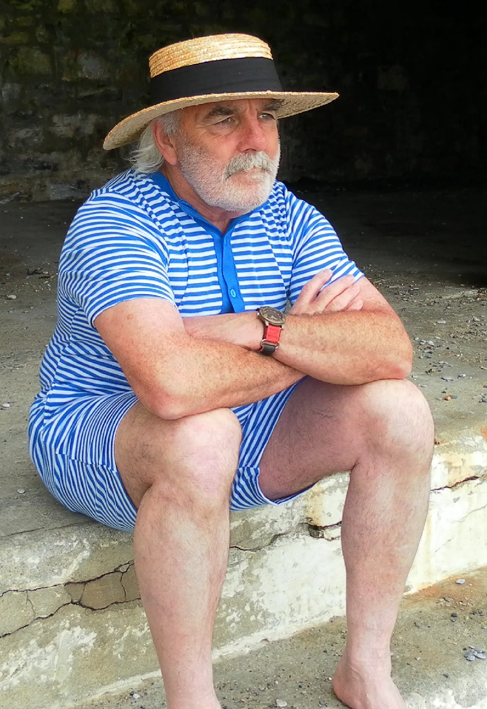 Pete Rendle sitting on steps in stripy outfit and straw hat