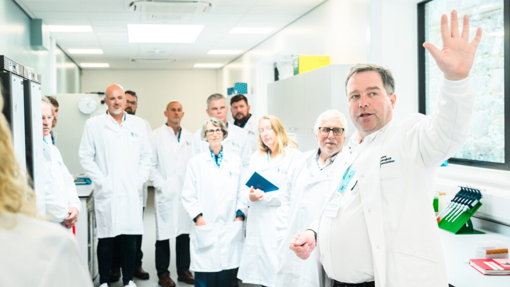 Official opening of the Marine Microbiome Centre of Excellence. CEO Professor Willie Wilson arm outstretched with group of visitors in lab coats.