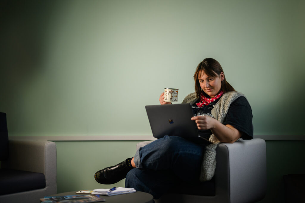 Cordelia Roberts sitting with a mug of tea reading from a laptop